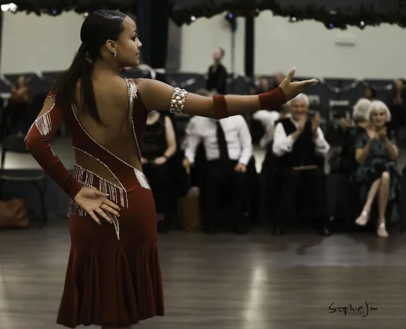 Dancer in a red costume posing for a seated audience, performing the cha cha taught in Ottawa dance classes