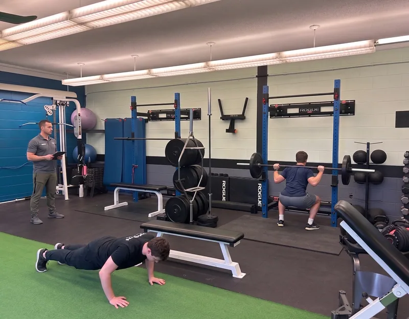 Gym floor with a squat rack, free weights and clients training under a coach at DQ Ballroom & Fitness in Ottawa