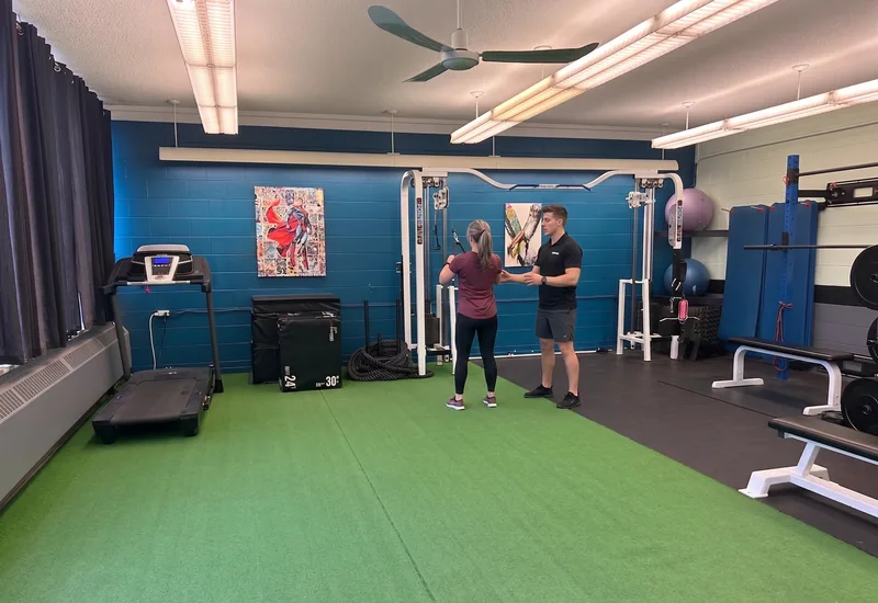 Trainer working with a client beside a treadmill and cable machine in the personal training room at DQ Ballroom & Fitness in Ottawa