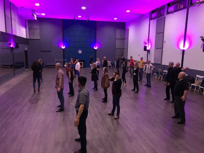 Group standing in a circle under purple lighting in a beginner salsa rueda dance class at DQ Ballroom & Fitness in Ottawa