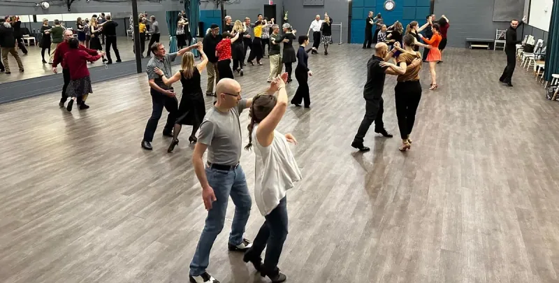 Couples spread across the floor learning partner moves in a beginner samba dance class in Ottawa at DQ Ballroom & Fitness