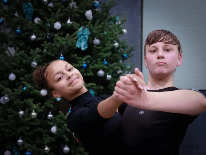 Two young dancers in black holding a connected frame by a decorated tree in an intermediate tango dance class in Ottawa