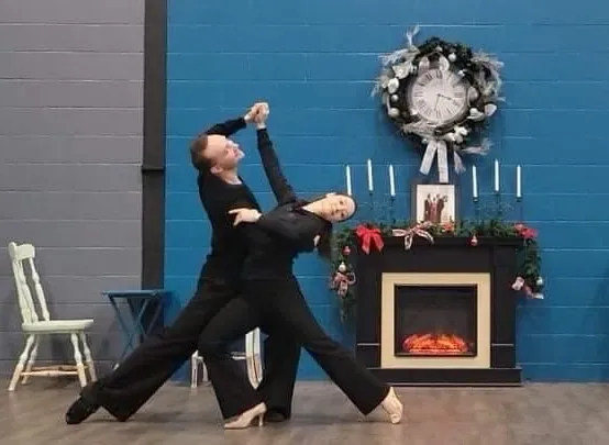 Couple in black practicing a waltz turn by a fireplace in an intermediate Ottawa waltz dance class